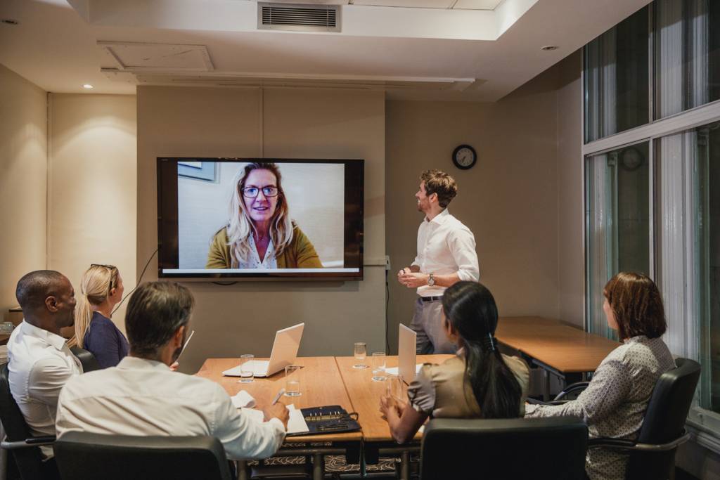 Meeting room with hybrid meeting set up showing one participant on meeting room screen joining remotely to illustrate how hybrid meetings make workplaces more inclusive for all.