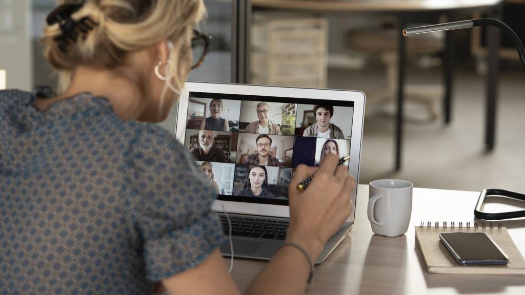 A blond woman with her hair tied up has her the back of her head to the viewer. She's talking and working on a video call with nine other participants.