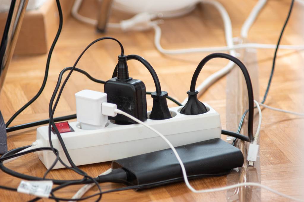 Messy outlet power extension cord on an apartment floor with various charging devices plugged in 2020