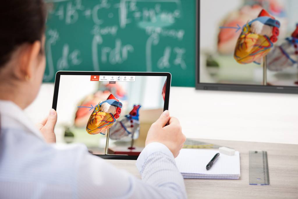 School child looking at a tablet that contains an image of the heart. This image is duplicated on the larger screen at the front of the room.