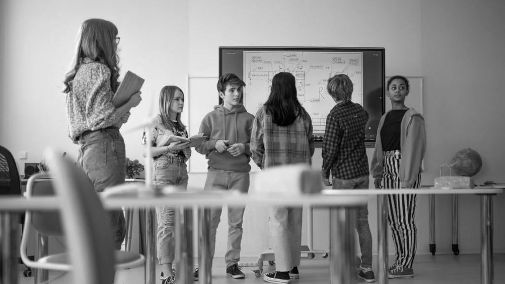 Teenagers in a classroom standing around an interactive whiteboard