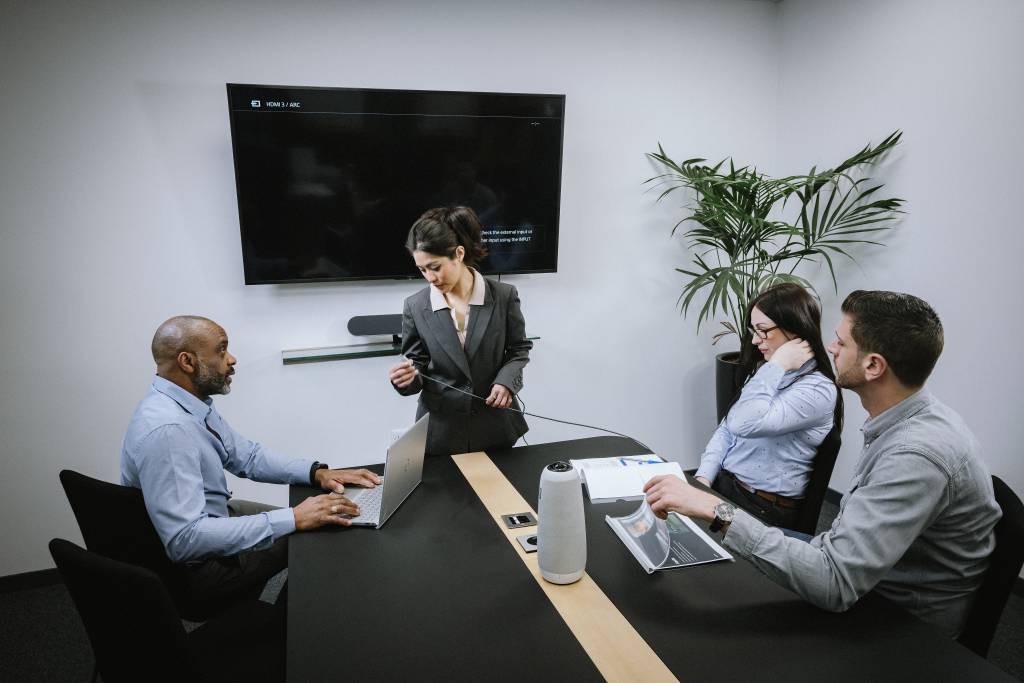 four people in a meeting room, struggling to connect devices and start a meeting